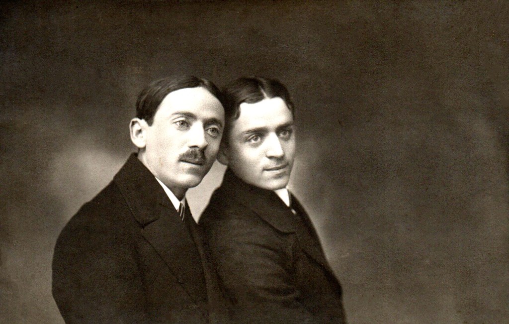 Sepia studio portrait of two young brothers in suits, their heads leaning together.