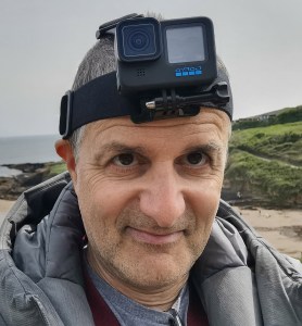 Michael Achtman outdoors on a coastline, wearing a GoPro camera strapped to his forehead.