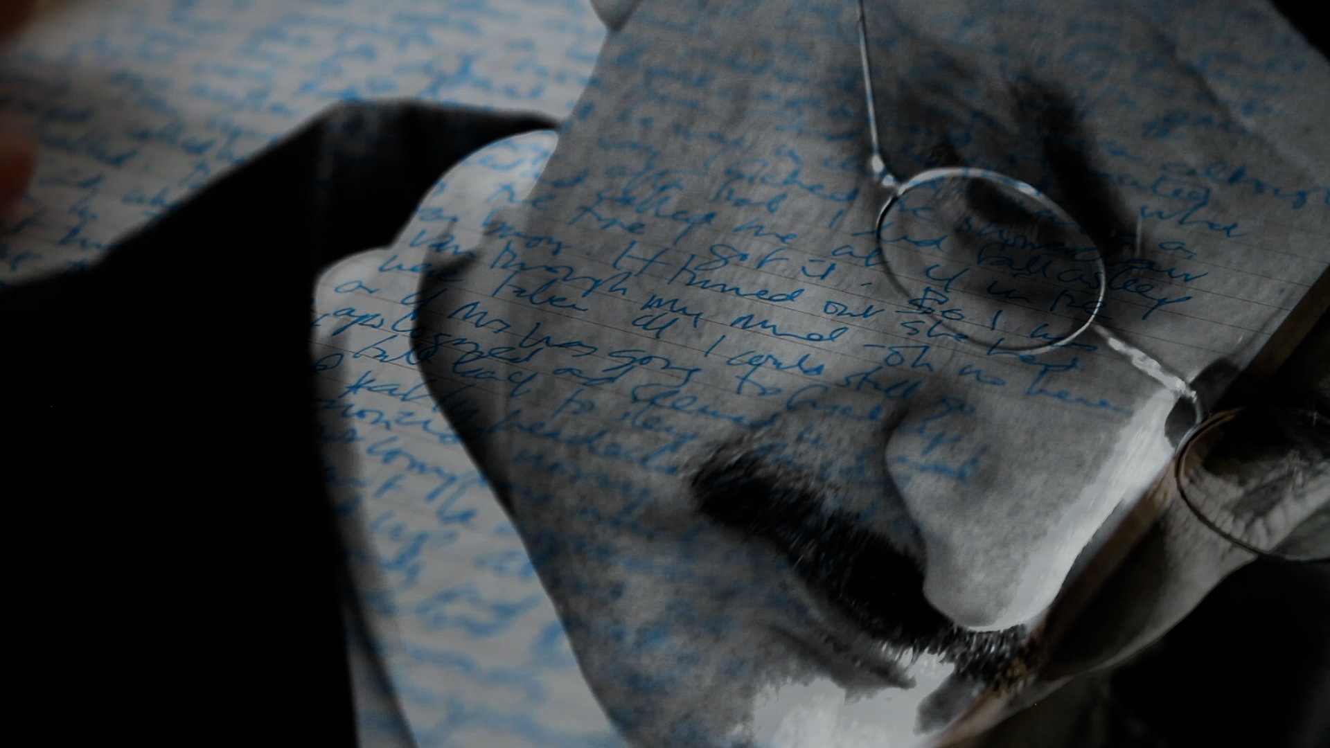 Double-exposed still from Pessoa: a close-up of a man wearing round glasses is superimposed over pages of handwritten notes, with a dark shadow crossing the composition.